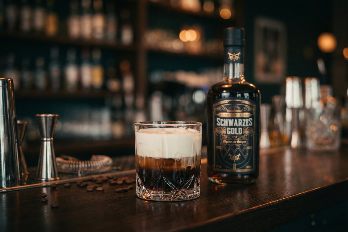 White Russian Cocktail mit Sahne-Schichtung und Schwarzes Gold Kaffeelikör auf dunkler Bar