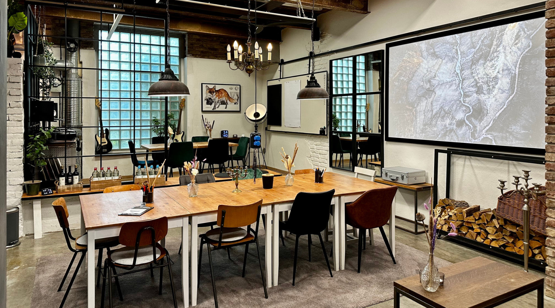 Seminarraum bei as/if spaces in Köln Nippes mit großen Holztischen, industriellen Lampen und einer Leinwand. Perfekt für kreative Meetings, Workshops und Seminare in inspirierender Atmosphäre.