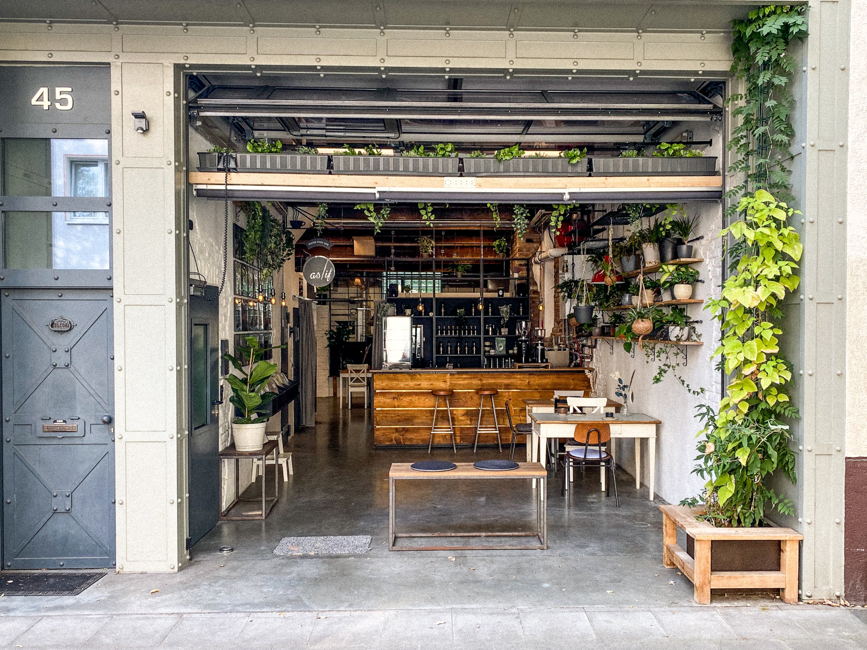 Offene Eingangstür von as/if spaces in Köln Nippes mit Blick auf die Espressobar und gemütlichen Sitzbereich, umgeben von Pflanzen. Perfekt für kreative Meetings, Seminare und Events in inspirierender Umgebung.